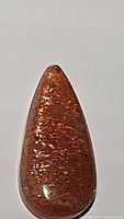 Close-up image of 14.45 carat natural pear-shaped sunstone cabochon showing reflective sparkling inclusions inside the polished brown-orange stone.