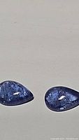 Photo of two teardrop-shaped purple-blue tanzanite cabochons with visible internal inclusions.