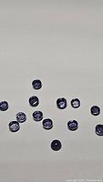Photo of 14 small round cabochon purple iolite gemstones spread on a white surface