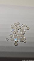 Photo showing multiple round cabochon rainbow moonstones with visible blue flash on a white background.