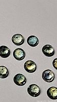 Twelve round tri-colored sapphires with green, blue, and yellow hues against a beige background.