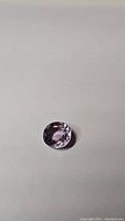 Oval-shaped bright purple Tourmaline gemstone on a plain background, showing clarity, cut, and color
