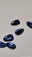 Seven pear-shaped royal blue kyanite gemstones on a flat surface showing their rich blue color and sparkle.