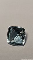 Close-up image of the cushion checker cut aquamarine gemstone showing its transparency and internal inclusions.