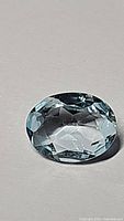 Oval faceted sky blue topaz gemstone shown on a plain background, highlighting clarity and color.