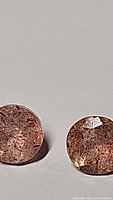 Clear close-up photo of two round strawberry quartz stones showing internal reddish inclusions and polished surfaces.