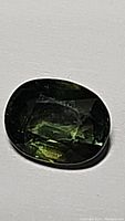 Close-up image of a polished oval green sapphire gemstone on a white background, showing good clarity and color.