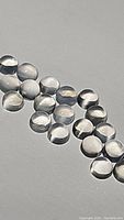 Photo of multiple small round white moonstone cabochons, showing their smooth, domed cabochon cut and translucent white appearance.