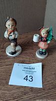 Photo of both Hummel figurines together showing boy with backpack and girl with tree and candle holder