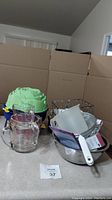 Overall view of bakeware including green silicone molds, glass measuring cups, metal mixing bowls, plastic measuring cup, and metal strainers on kitchen counter.