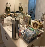 Bathroom countertop with stainless steel toilet paper holder, dental hygiene products, framed seashell art, and decorative items.