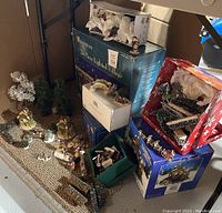 Wide shot of many Christmas village items including boxed buildings, trees, and figurines arranged on floor.
