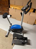 View of entire exercise bike and manual stepper on floor with furniture in background.