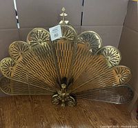 Full view of brass fireplace screen in opened peacock fan configuration on wood floor.