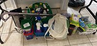 Wide shot of all cleaning supplies including two steam mops, cleaning bottles, brushes, and wipes arranged on tile floor.