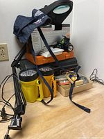 Photo of rechargeable battery charger with batteries, cordless screwdriver kit, handheld flashlights, magnifying lamp, some hand tools and hardware on table.
