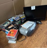 Hisense LCD TV, Sony tape/radio player, lots of cassette tapes, CDs, and DVDs displayed on wooden floor.