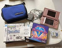 Overview photo showing pink Nintendo DS Lite, charger, 7 games, and blue carrying case on white surface.