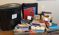 Wide assortment of office and stationery items organized on a desk surface, shows bins, notebooks, tapes, labels.