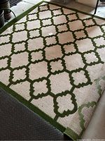 Full view of cream-colored indoor/outdoor rug with green geometric quatrefoil pattern and solid green border.