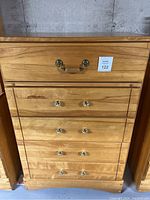 Front view of the tallboy dresser showing five drawers with different handle styles and some scratches.