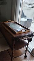 Wooden tea cart with removable serving tray on top next to sliding glass door.