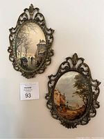 Pair of vintage Italian oval ornate brass frames with scenic paintings hung on wall, showing overall look and size.