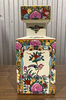 Front view of the square ceramic vase showing colorful floral and bird motifs with a cream background.