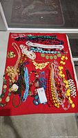 Full view of costume jewelry necklaces laid on red cloth showing various colors and bead types.