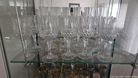 Set of 11 smaller crystal glasses and 6 champagne flutes displayed on a glass shelf.