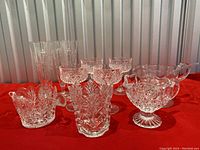 Full view of glassware and serveware items including glasses, condiment dishes, pitchers, and ladle on red cloth