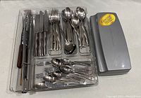Full view of cutlery set organized in clear storage tray alongside electric carving knife case.