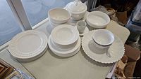 Photo showing full set of white dinnerware and servingware including dinner plates, bowls, tureen with lid, cups, saucers, and serving tray on a table.
