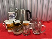 Electric kettle, various glass mugs, ceramic mugs, drinking glass, and shot glass arranged together