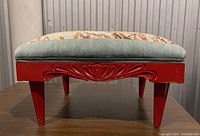 Front view of wooden footstool showing red painted wood with carved accent and light blue cushioned top