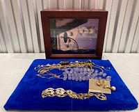 Wood photo display box with glass front and costume jewelry necklaces and pin arranged on blue velvet background.
