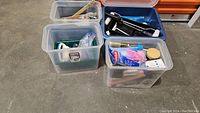 Four plastic storage bins containing various painting and cleaning supplies on the floor