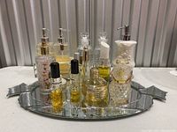Photo showing an arrangement of various glass perfume and cologne bottles, clear and ceramic soap dispensers on an oval mirrored tray.