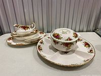 Photo shows the china set including divided serving dish, lidded casserole, gravy boat with underplate, trinket dish, and platter all with Old Country Roses pattern and gold trim.