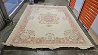Full view of large rectangular wool pile rug with a central medallion and floral border.