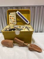 Open yellow plastic sewing kit showing interior compartments filled with sewing supplies and McCall's Easy Sewing book, along with wooden shoe stretchers outside.