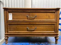 Front view showing two drawers with decorative metal handles and the overall rectangular wooden structure on four legs.