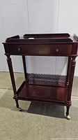 Front view of the wooden tea cart showing drawer, shelves, turned legs, and brass casters