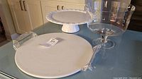 Photo showing the white ceramic pizza stone with handles, clear glass trifle bowl on pedestal, and white pedestal cake plate.