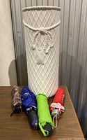 Front view of white ceramic umbrella stand with 4 folded umbrellas in front in black floral, blue, green, and red