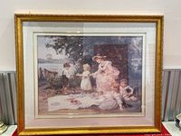 Full view of the framed print depicting a woman and children in a garden scene with a picnic blanket and treats.