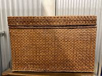 Closed view of the rectangular wicker chest showing woven pattern and areas with broken wicker strands especially along bottom front edge.