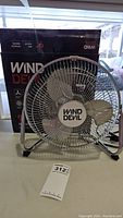 Front view of Wind Devil 9 inch high velocity industrial fan with metal blades and chrome frame, including original box in background.