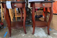 Two round wooden side tables placed side by side showing front, legs, lower shelves, and drawers, with visible signs of wear and scratches