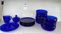 The full set of blue glassware including bowls, plates, creamer, and covered dish shown stacked and arranged on a table.